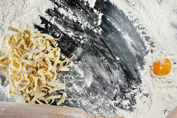 Fresh pasta noodles and flour on a dark surface with warm yellow tones